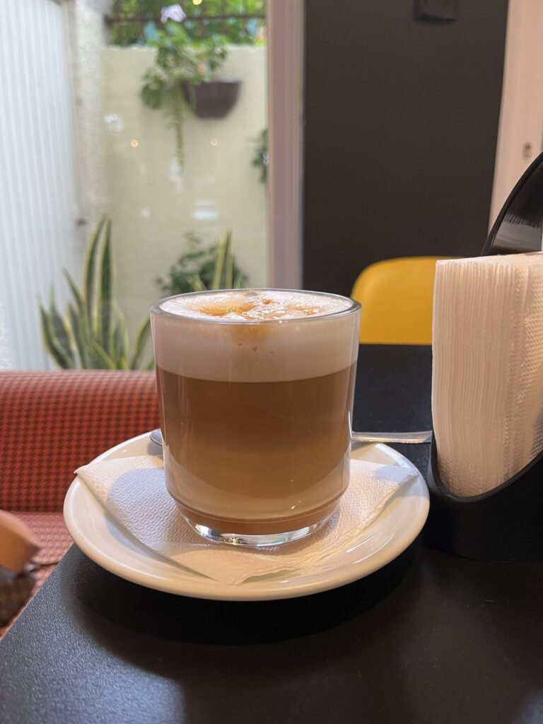 Xícara de café com leite espumoso em copo de vidro. Momento relaxante da psicóloga clínica Pauline Salvagni.